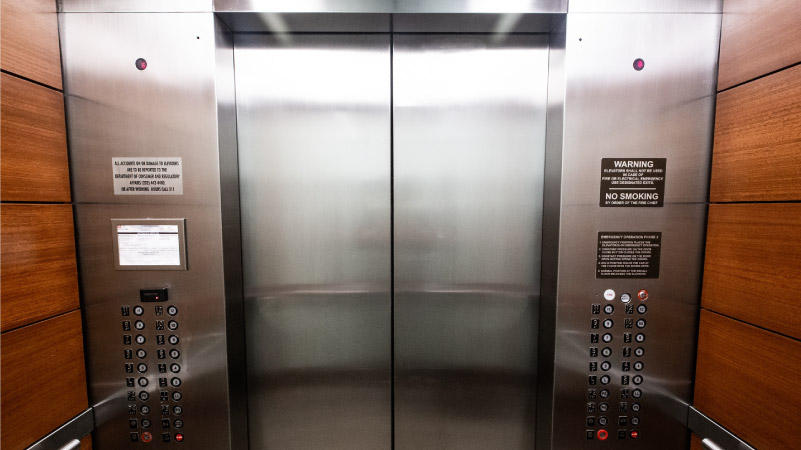 View of a stainless steel elevator door from inside a wood-paneled elevator.
