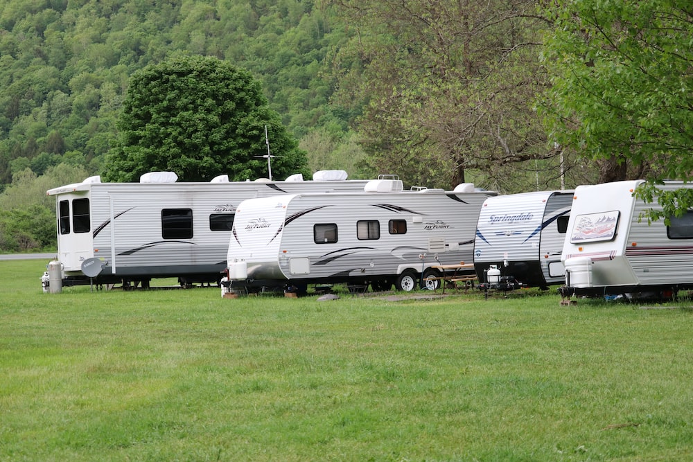4 RV trailers of varied colour on a green grass field during daytime.