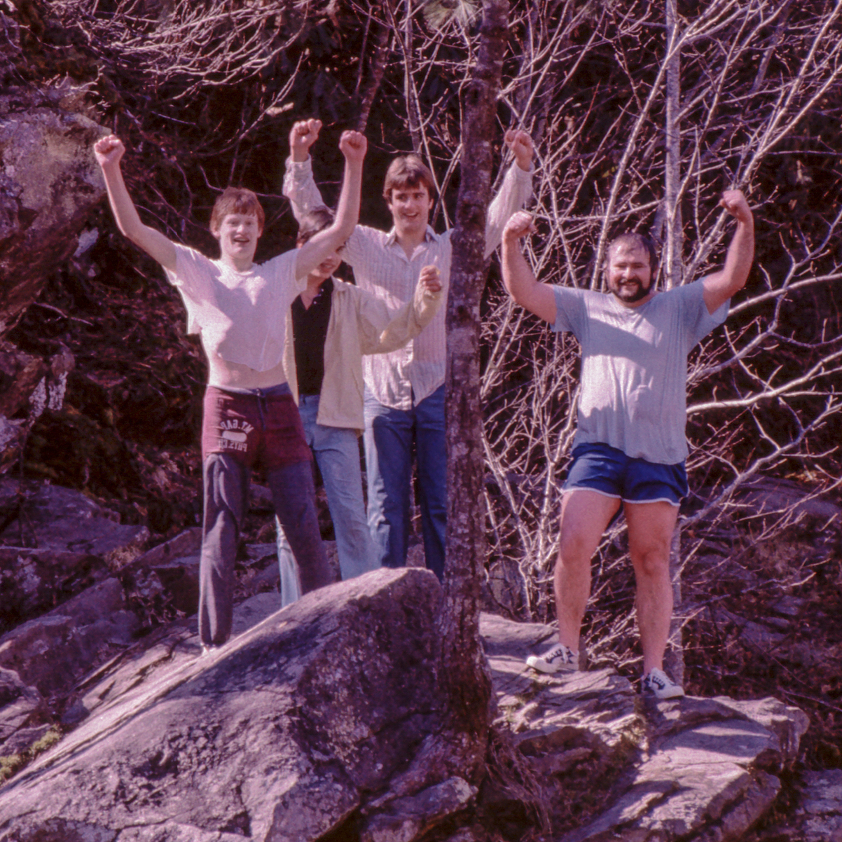 Four men hold their arms up standing on a rock. 
