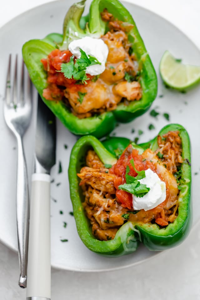 Chicken stuffed peppers on a white plate topped with pico de gallo and sour cream