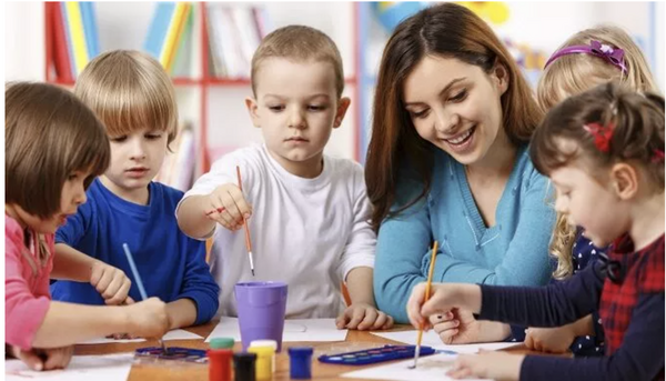 Teacher seated together with children painting
