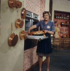 Woman placing a large dish into an open open at waist height. On wall are hanging copper pots.