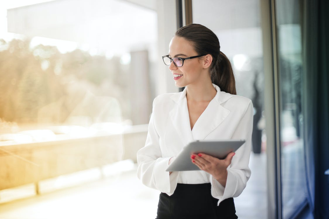 Quanto custa uma consultoria empresarial: profissional mulher com seu tablet olha pela parede de vidro