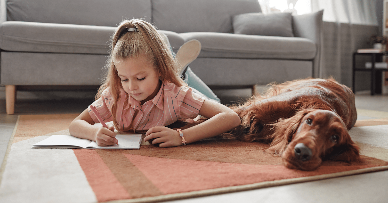 Girl laying on floor next to dog while writing in notebook