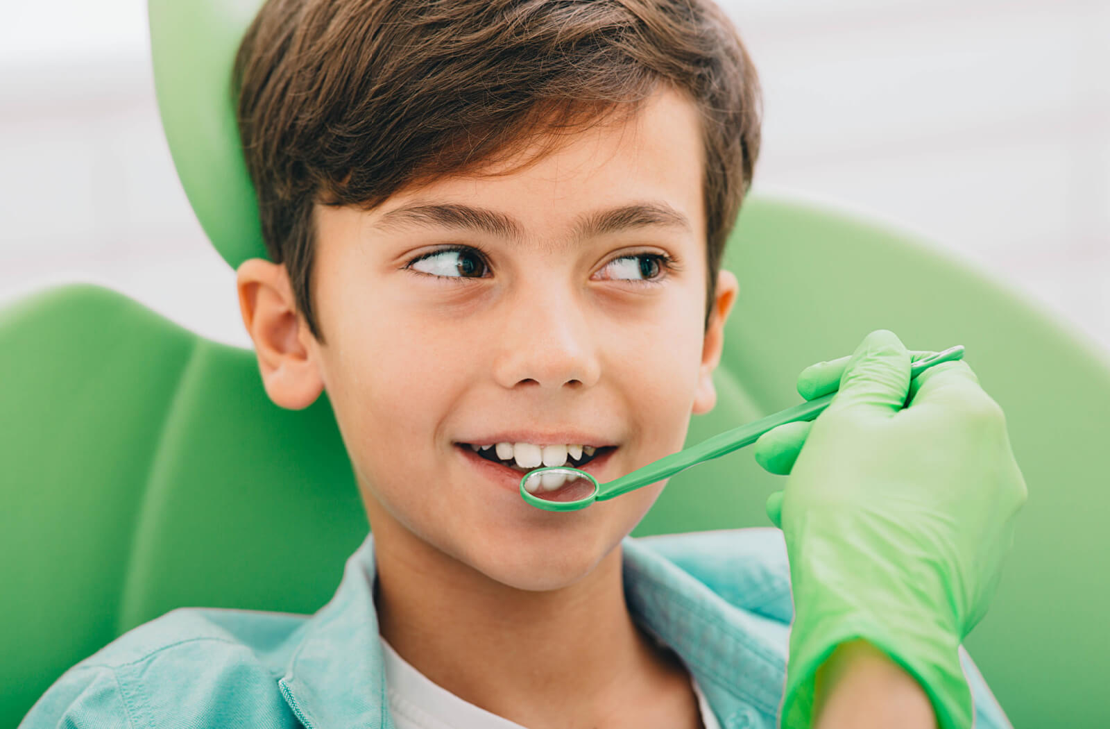 A dentist checks their young patient's teeth using a dental mirror