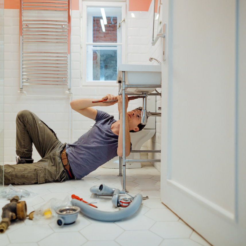 A plumber lying on the floor under a sink