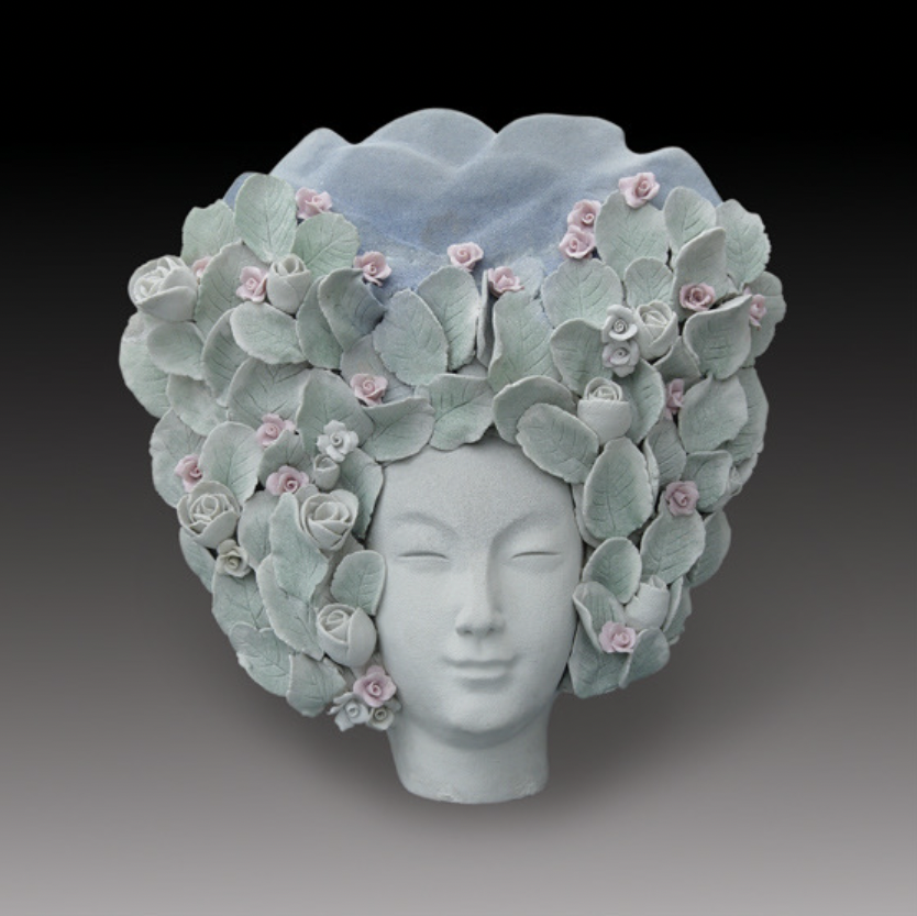 Image: Work by Jin’s mother, Qing Yang. A sculpture of a person's face, gentle green. Surrounding their face, like hair, are leaves and pink roses. Image courtesy of artist. 