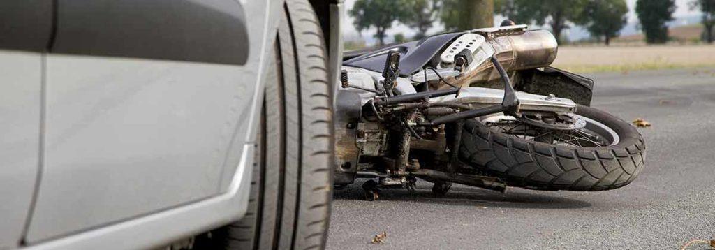 A motorcycle lies on its side in front of a silver car after an accident.
