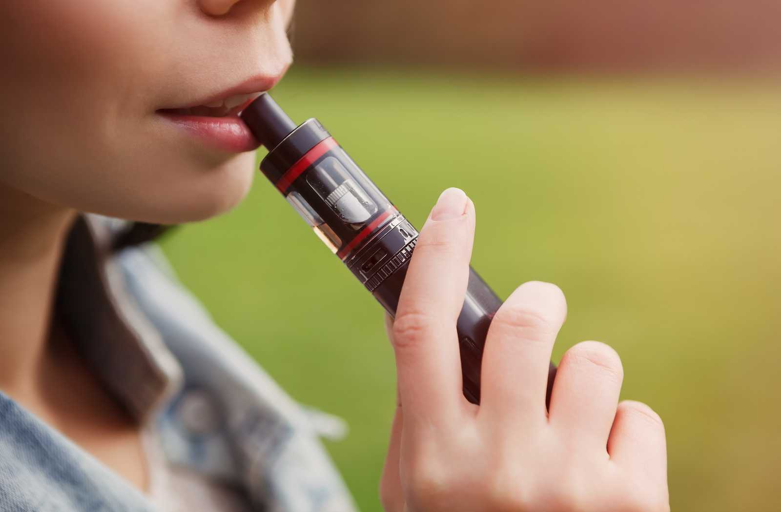 close up of woman vaping on a green background