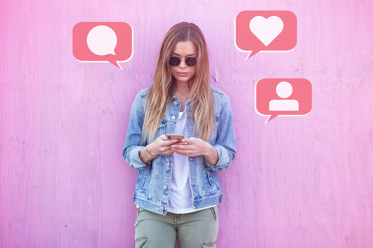 Influencer wearing sunglasses checking social media on their phone in front of a pink wall.