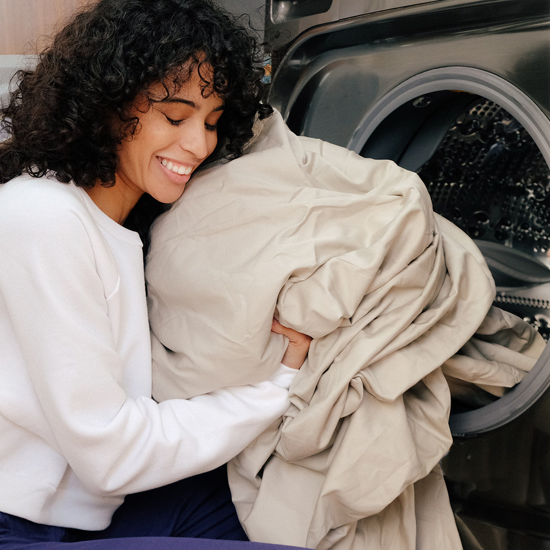 Young woman getting the newly washed sheets from the front-load washing machine.