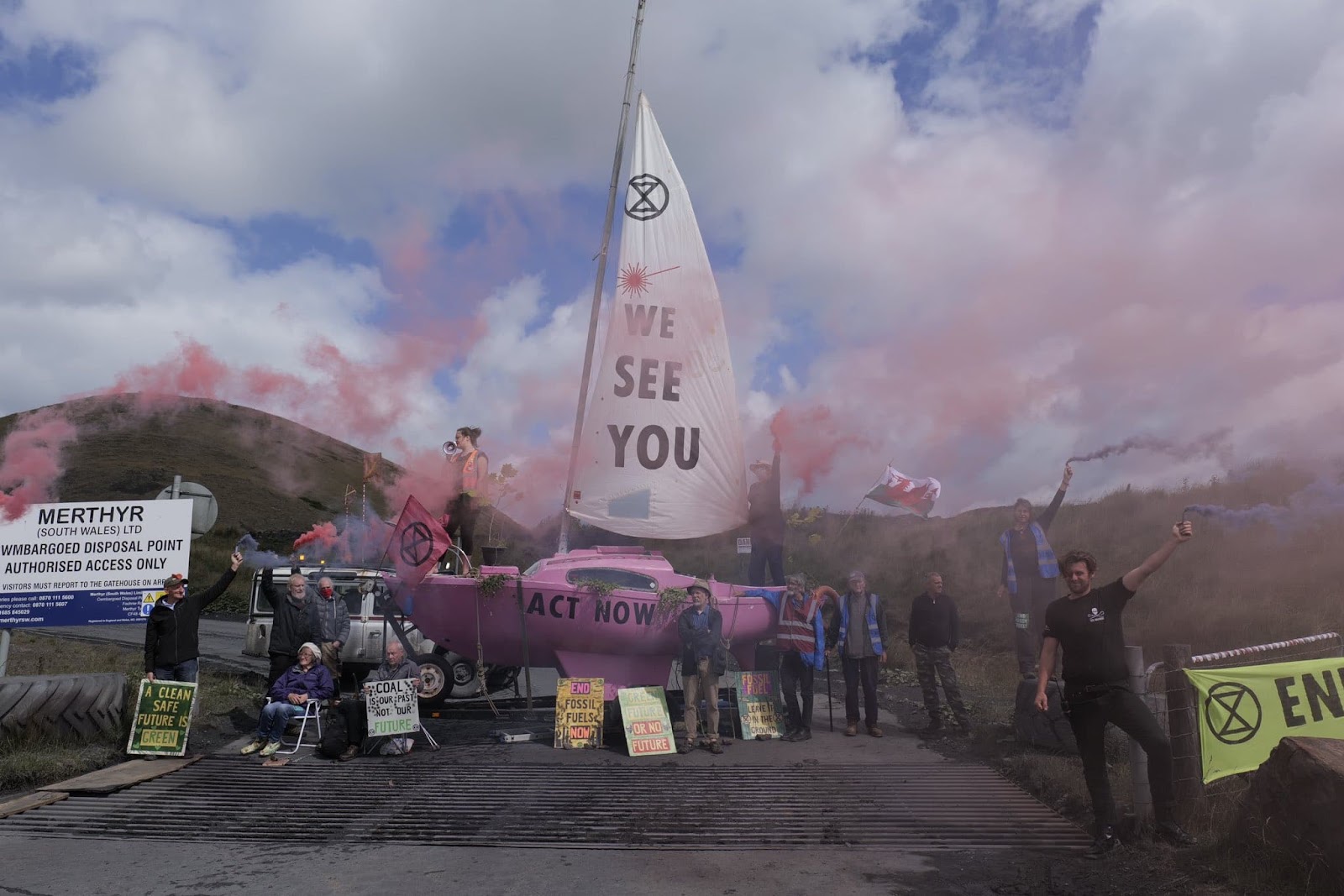 A rebel with a megaphone stands atop the pink boat while rebels let off smoke flares around it