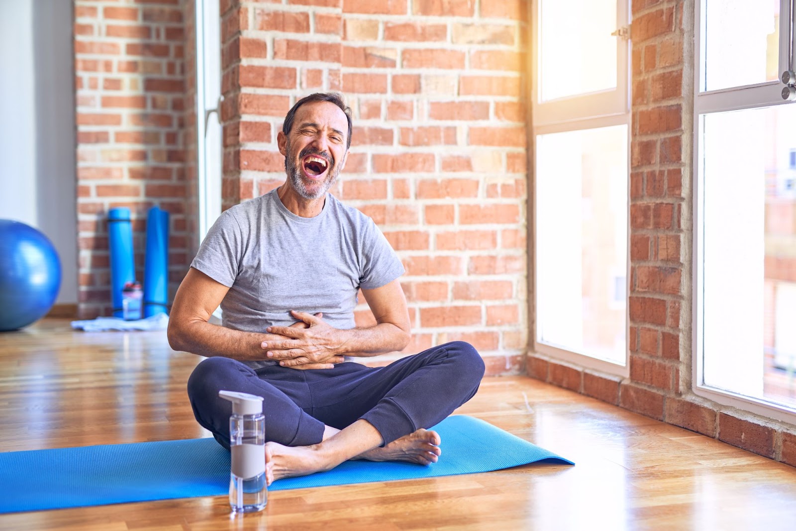 A man sat on a yoga mat laughing. 