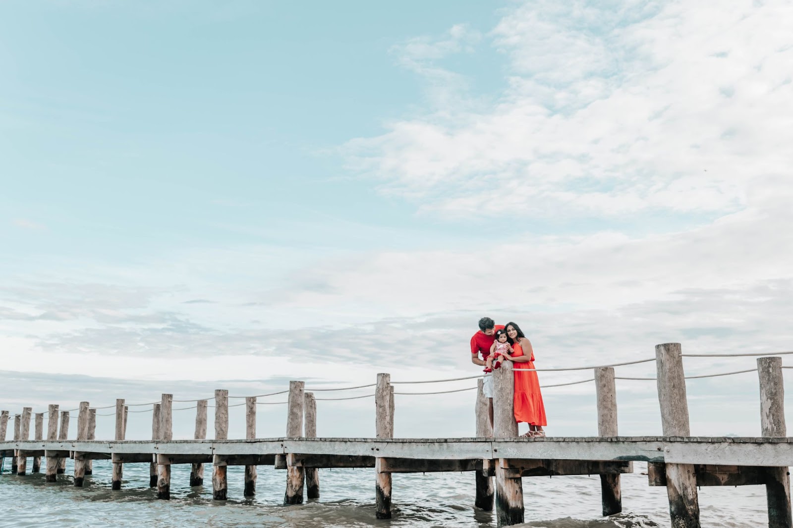 women in red dress with a young child for maternity shoot and men wearing neutral at a Jetty around Sydney