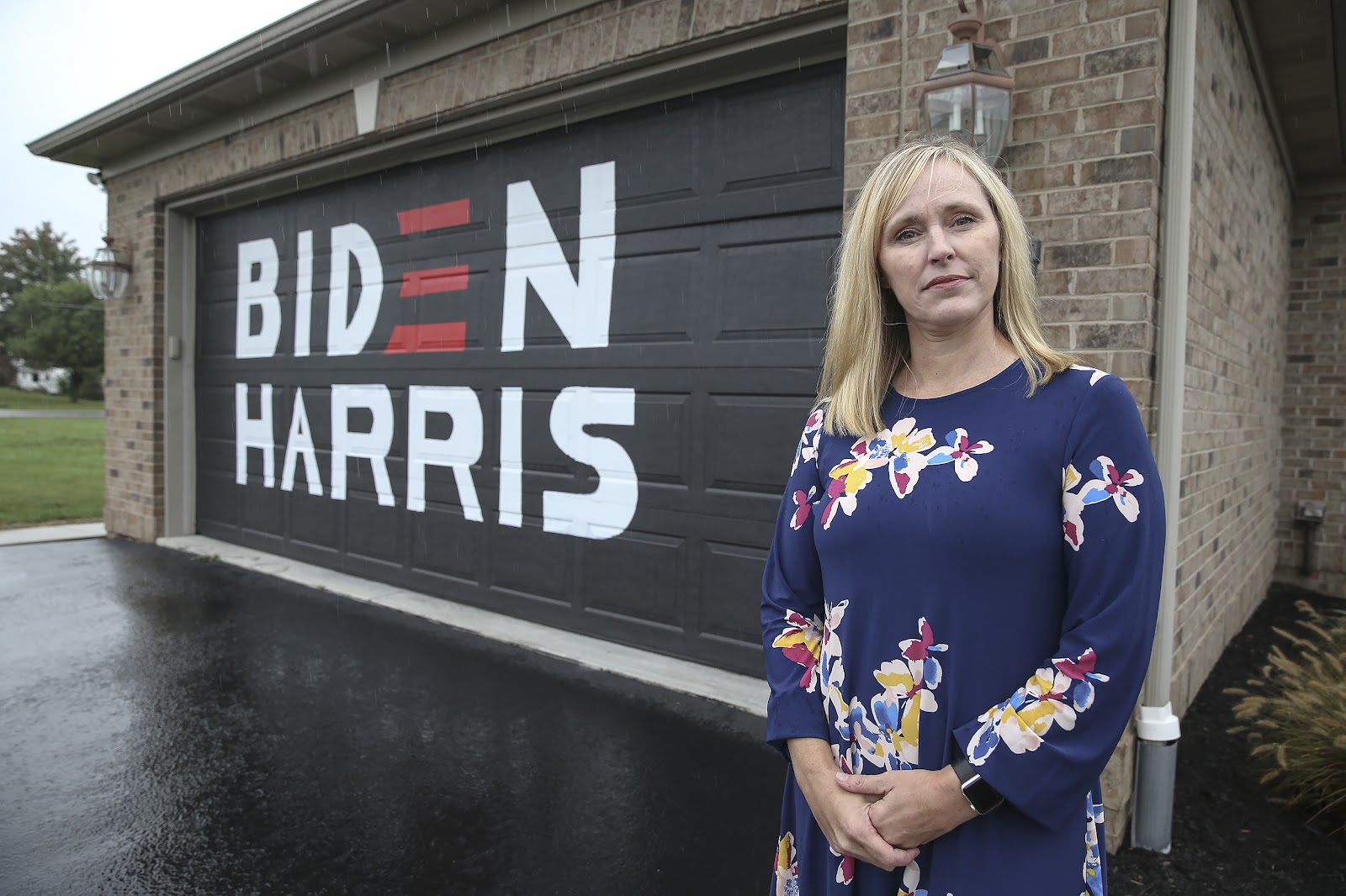 A woman posing next to her garage with the door painted Biden Harris' logo