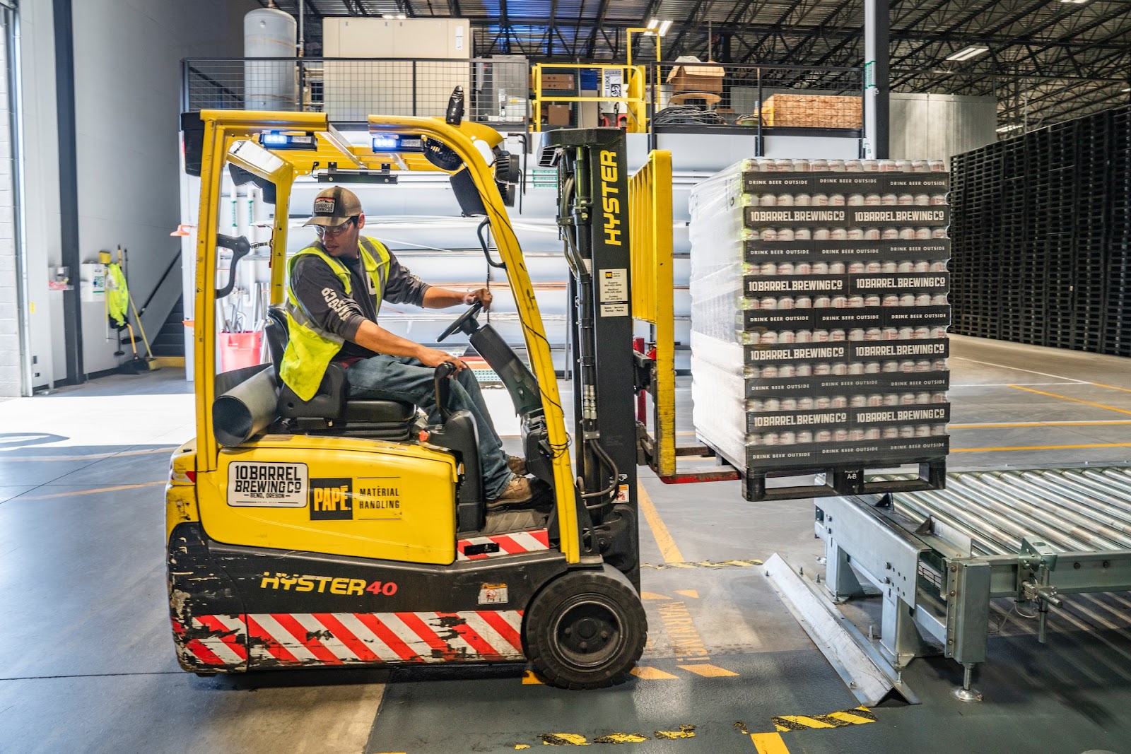 A worker uses a forklift to move pallets of cans.