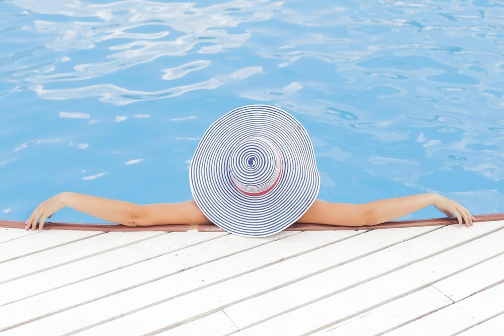 woman leaning on white concrete surface beside swimming pool during daytime