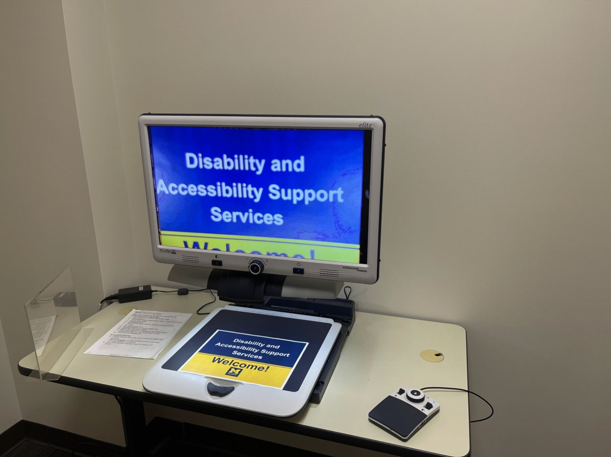 Video magnifier located in the DASS office. The device is sitting on a desk top with a sheet of paper under its camera. The screen is displaying the text "Disability and Accessibility Support Services."