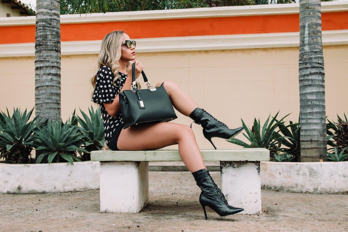 Free Woman Wearing Black and White Polka-dot Shirt With Black Short Shorts Holding Black Leather Tote Bag Sitting on White Concrete Bench Stock Photo
