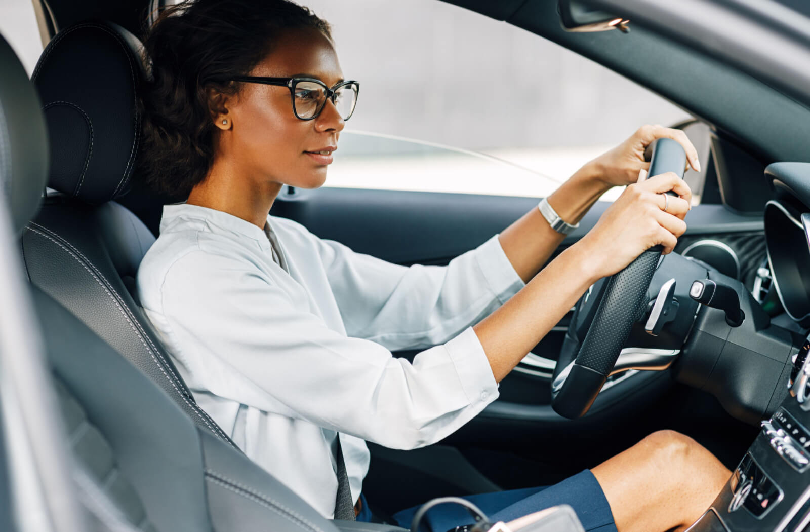 A lady is wearing anti-reflective coated eyeglasses while driving her car.