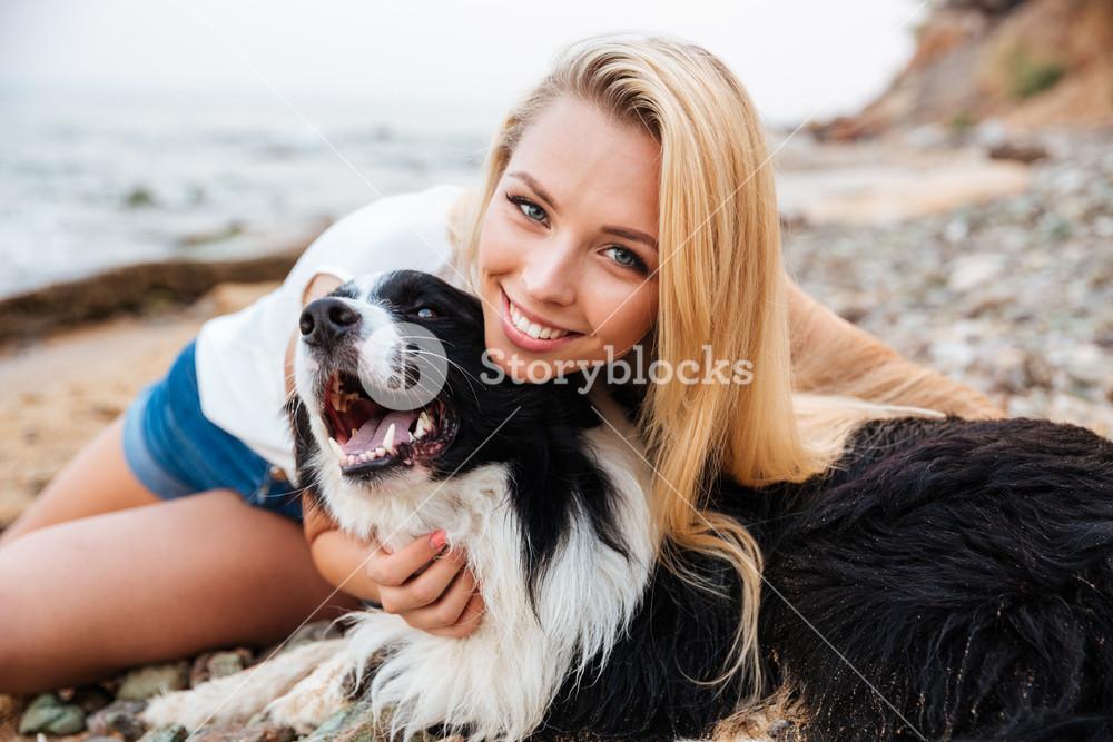 Cheerful pretty young blonde woman sitting and hugging her dog on the beach  Royalty-Free Stock Image - Storyblocks