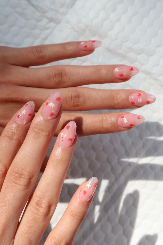#DescriçãoDaImagem: mãos com foco nas unhas que estão pintadas de cor de rosa claro com detalhes em vermelho e branco. Foto: Pinterest.