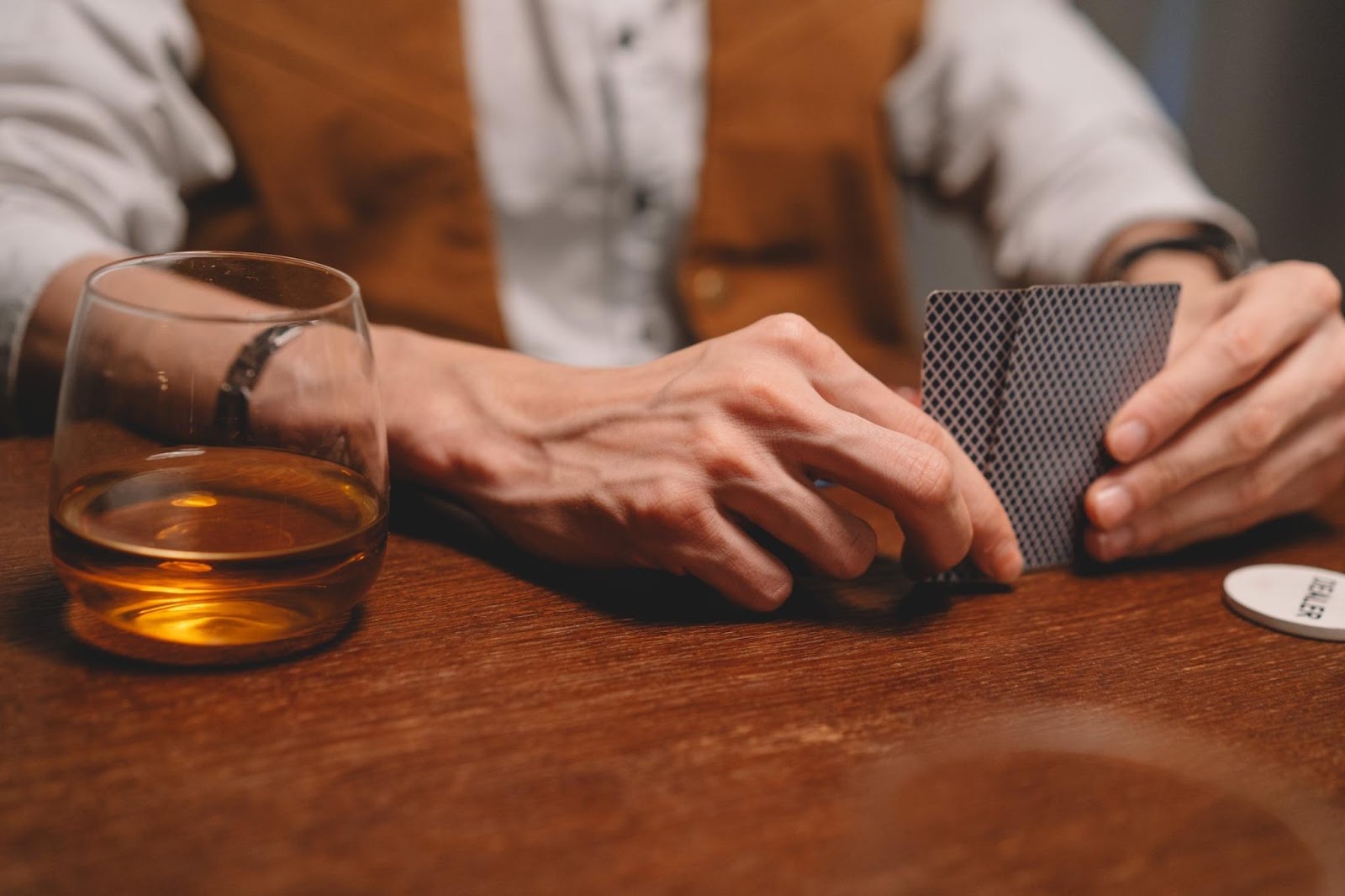 A man playing poker with a glass of whisky to his right.