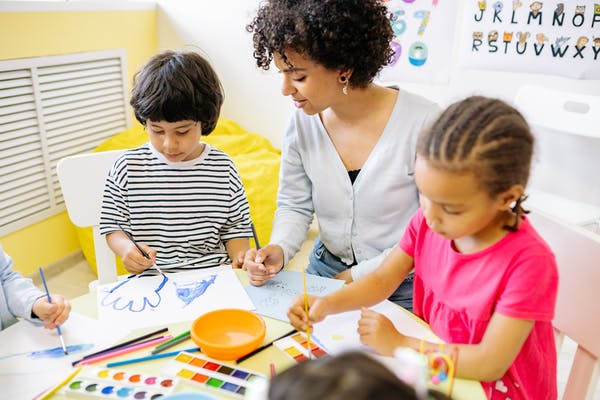 Preschool teacher sitting at table with children painting 