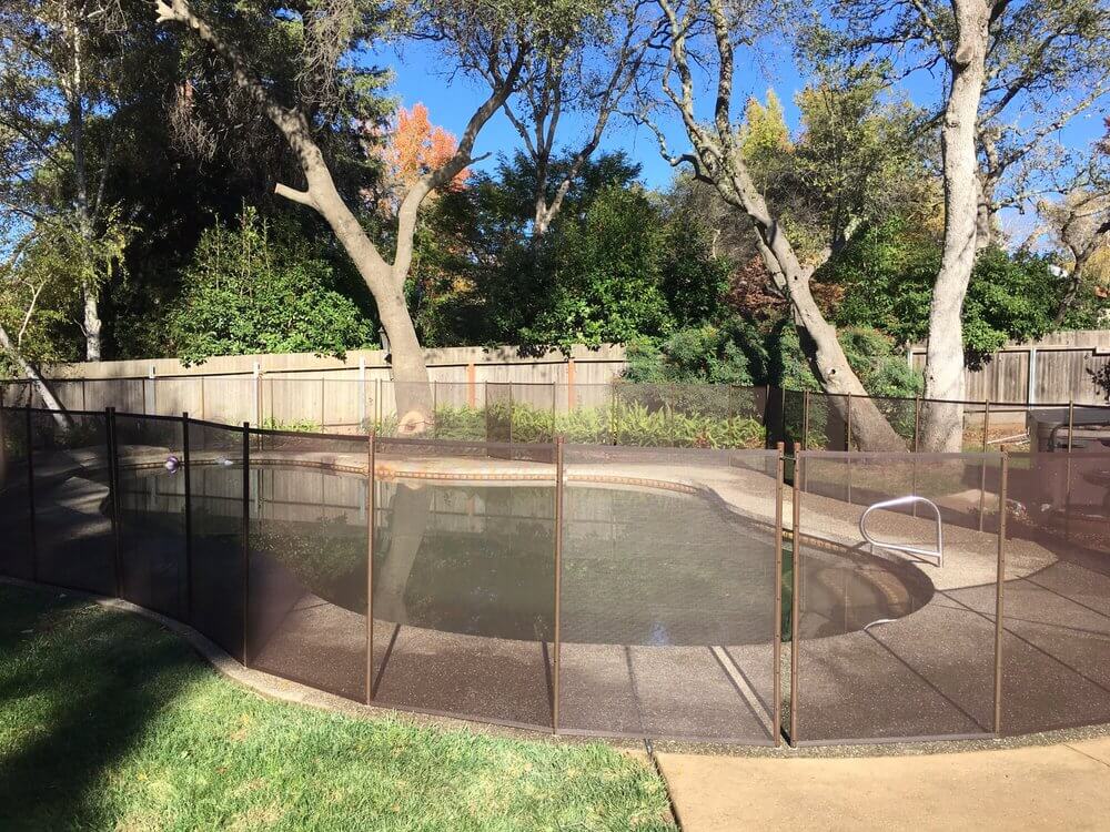 Brown mesh swimming pool fence installed around a backyard pool