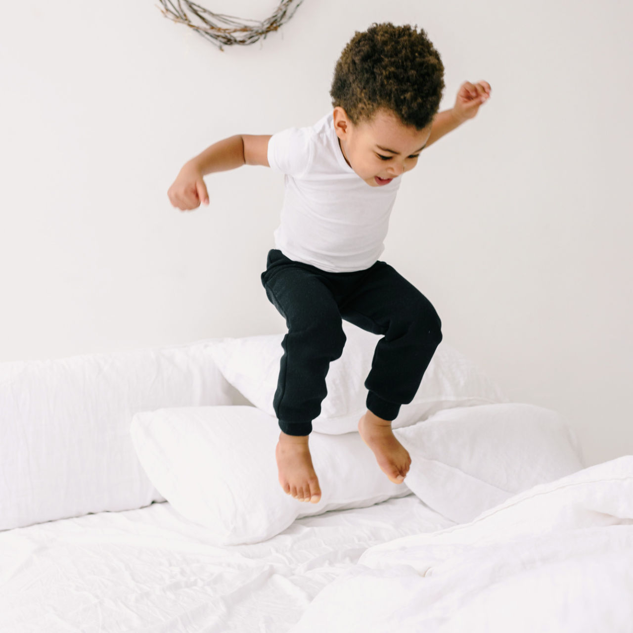 A boy jumping happily on a white bed.