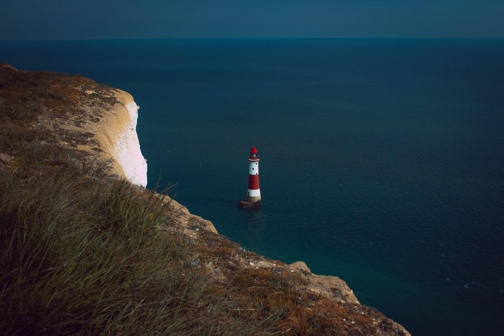 red and white lighthouse on cliff near body of water during daytime
