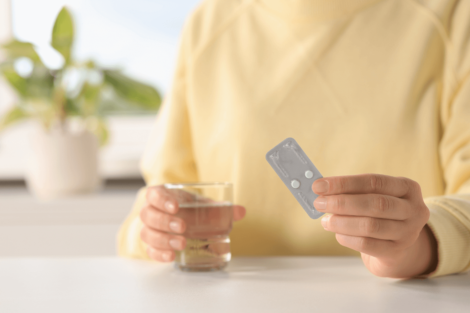 Woman holding a glass of water and a pill pack with two pills