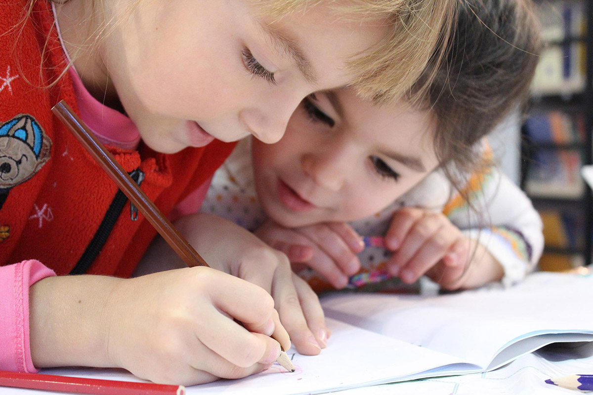 2 children working on a school assignment holding pencils and looking at their worksheet