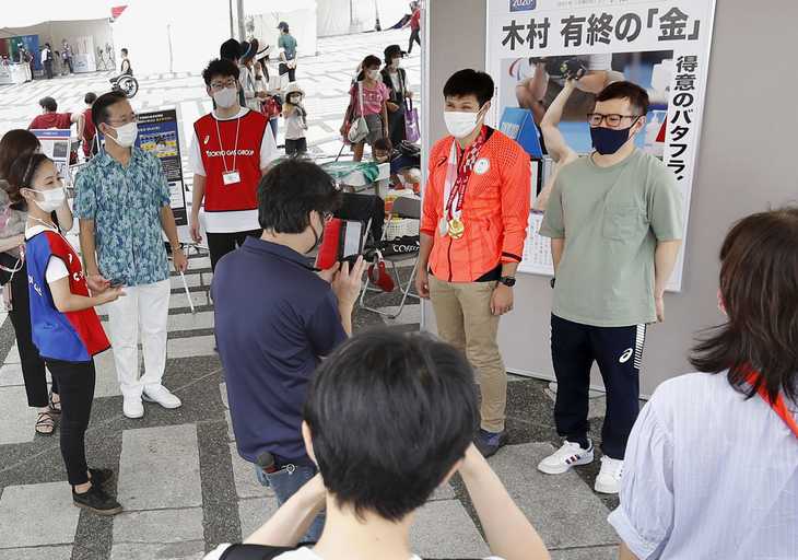 東京パラ競泳金メダリストの木村敬一選手（奥右から２人目）と記念写真に納まる来場者＝２０日午前、東京都世田谷区の駒沢オリンピック公園