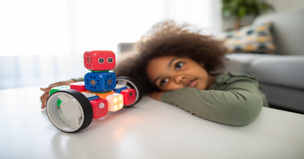 Small business holiday gift guide–An image of a child with curly hair leaning on a table playing with a red and blue robot toy. 