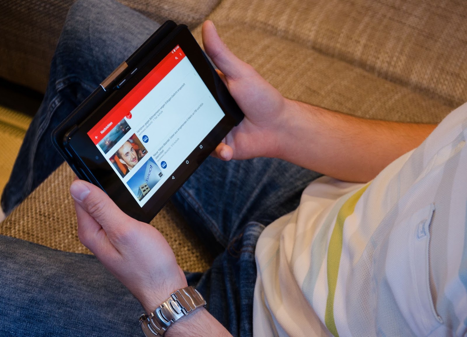 A man sits on the couch watching youtube on a tablet.