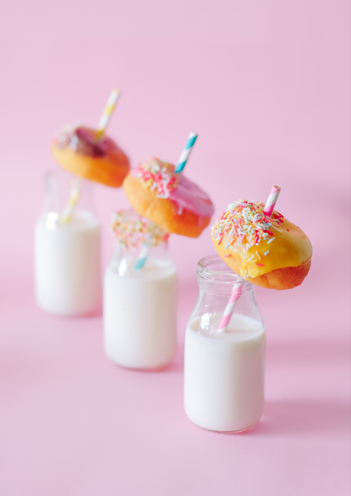 Glass bottles of milk with colorful straws and frosted donuts are pictured on a pink background. A dessert bar is another creative use for our mobile bar, Pearl.