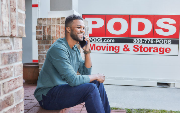 A man talking on his phone with a PODS moving container in the background