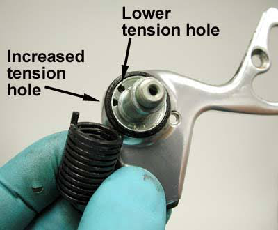 The tension of the derailleur can be changed by removing a tension spring from one opening and putting it into another.