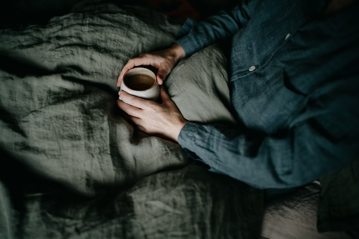 A man sat in bed holding a warm drink
