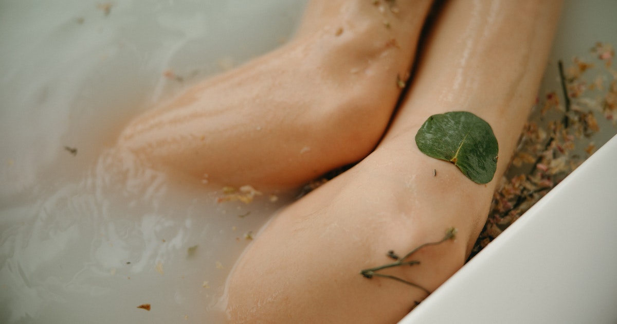 Woman soaking her legs in warm milky bath containing herbs 