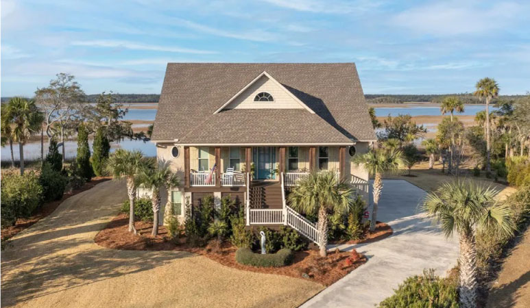 A gorgeous, two-story waterfront home in Brunswick, Georgia, with a big open yard and several palm trees on the property.