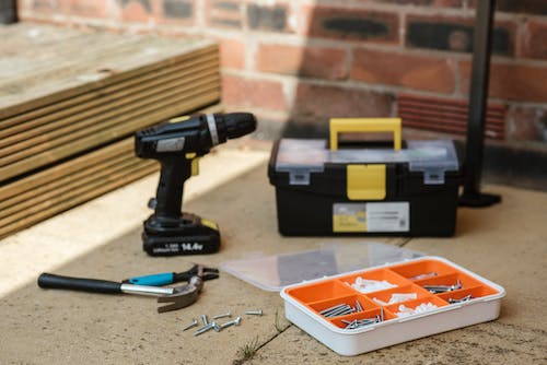 Free Electric screwdRiver on floor near containers with instruments placed near spanner with hammer against brick wall  and wooden barrier Stock Photo