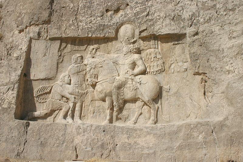 Large wall carving in rock depicting the defeat of the Roman emperor before the Persian king Shapur I on horseback.
