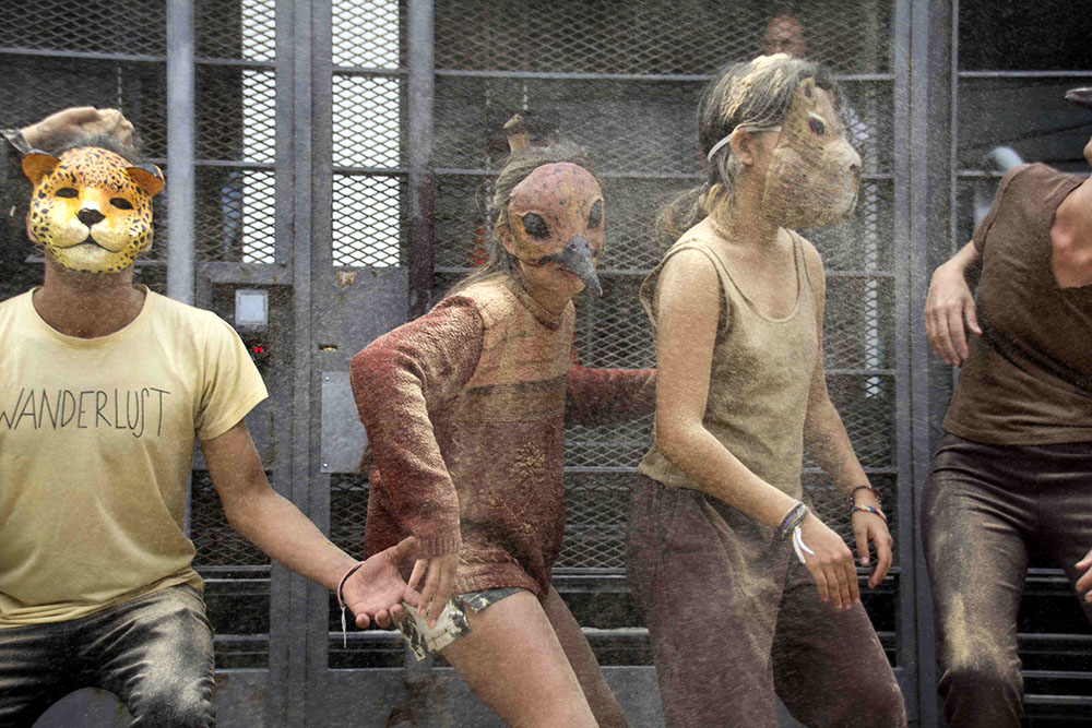 Rebels wearing animal masks dance in front of a metal grille