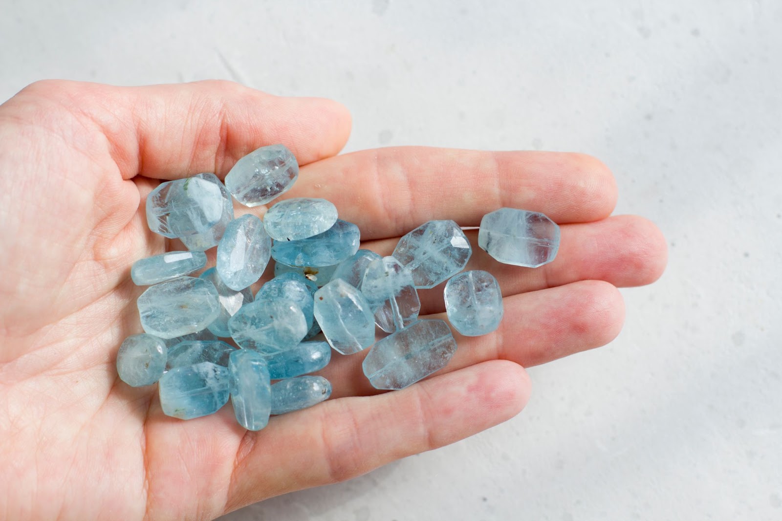 An open palm holding many bright blue aquamarine crystals. 