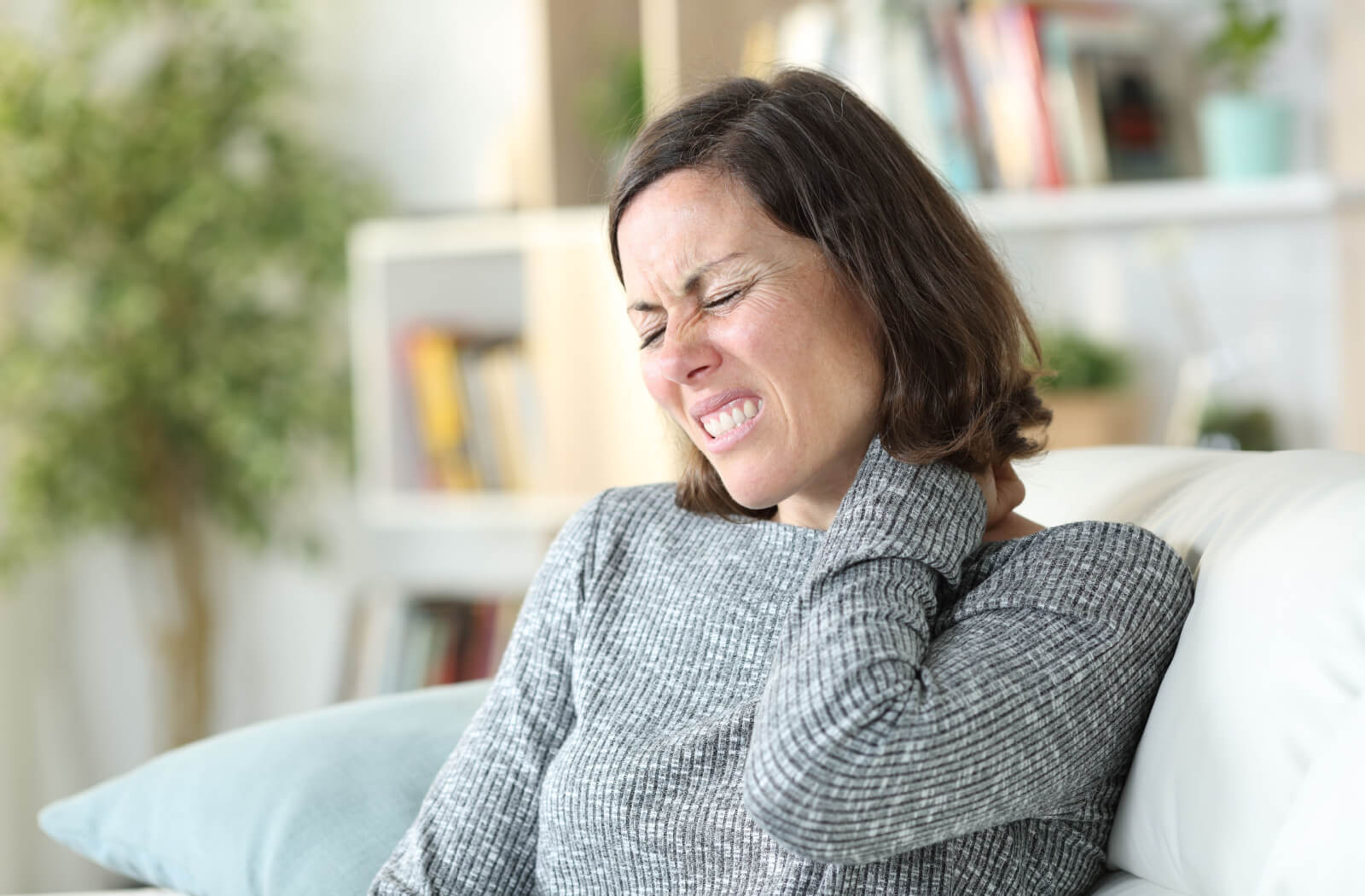 A woman in a grey sweater suffering from severe neck pain.