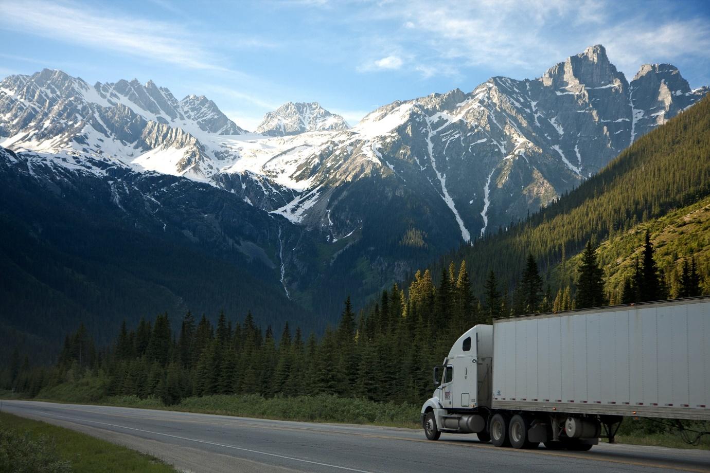 a large white interstate moving company truck driving along a road with mountains