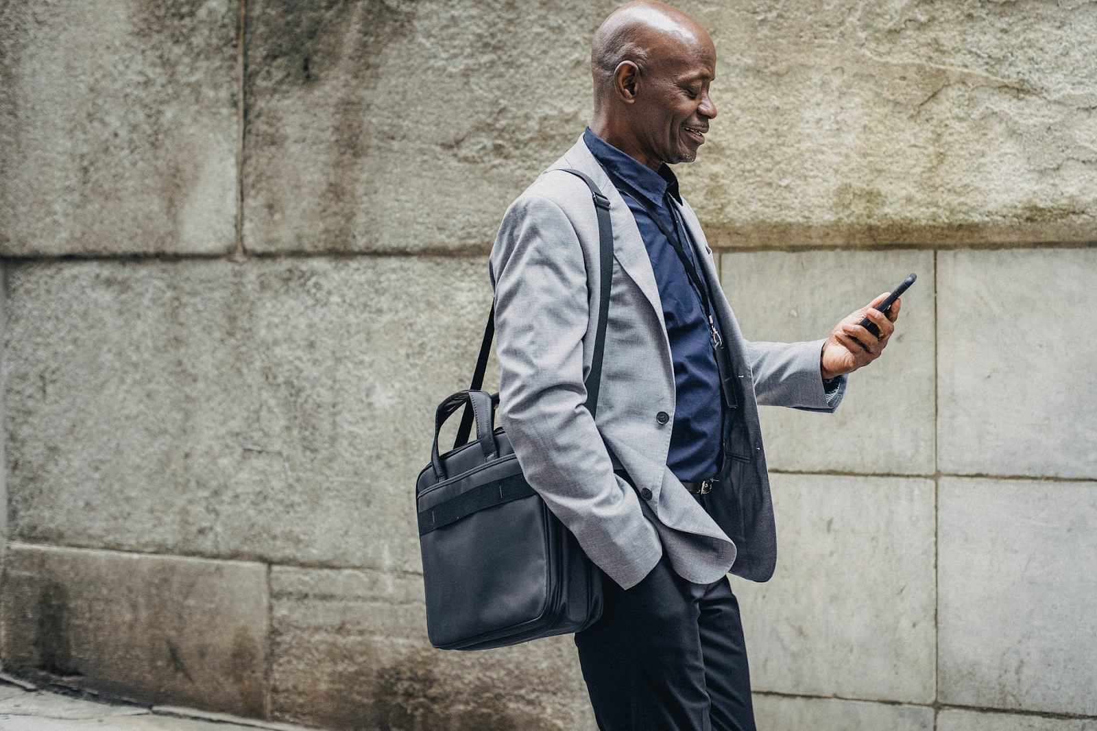 Cheerful black manager looking at smartphone while walking down street