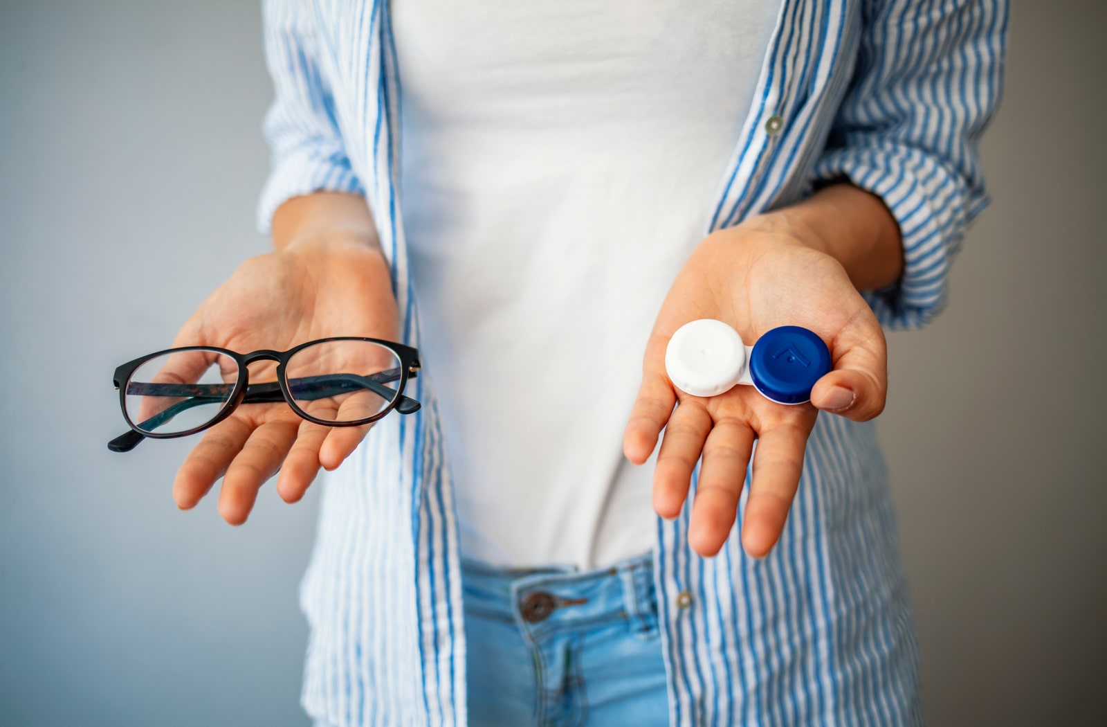 A woman holding on to a pair of glasses in her right hand and a contact lens case in her left hand